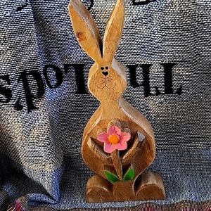 Little Easter Bunny carved out of wood with holding a pink flower in his hands